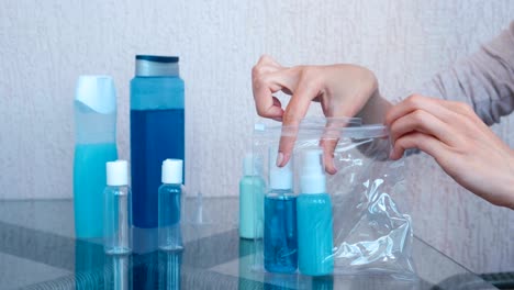 las manos de las mujeres ponen un conjunto de cosméticos con botellas y frascos en una bolsa de plástico con cremallera. frascos de primer plano.