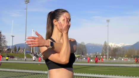 joven atlética estirando los brazos al lado del campo antes de entrenar