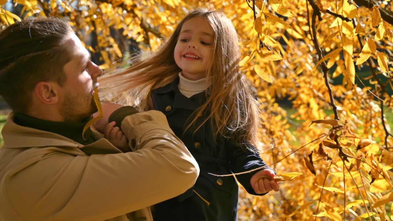 Happy family in an autumn park. Father took his daughter in his arms and she kissed him near a yellowed tree. Slow motion