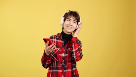 A young woman enjoying music with headphones and her smartphone on a yellow background