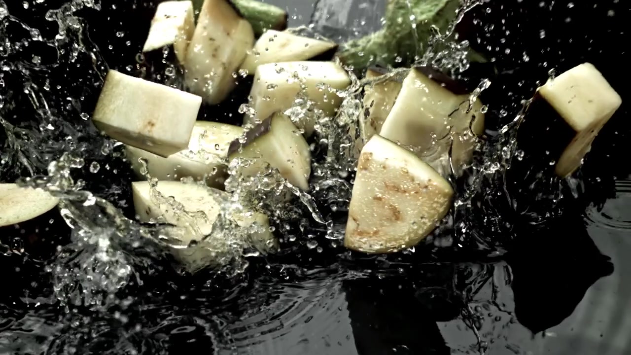 Morceaux d'aubergine fraîchement coupés éclaboussant dans l'eau au ralenti