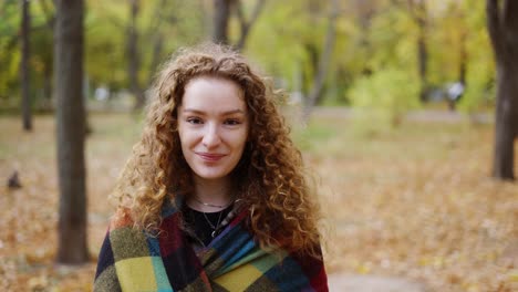 portrait of beautiful curly young woman in and autumn park covered with plaid