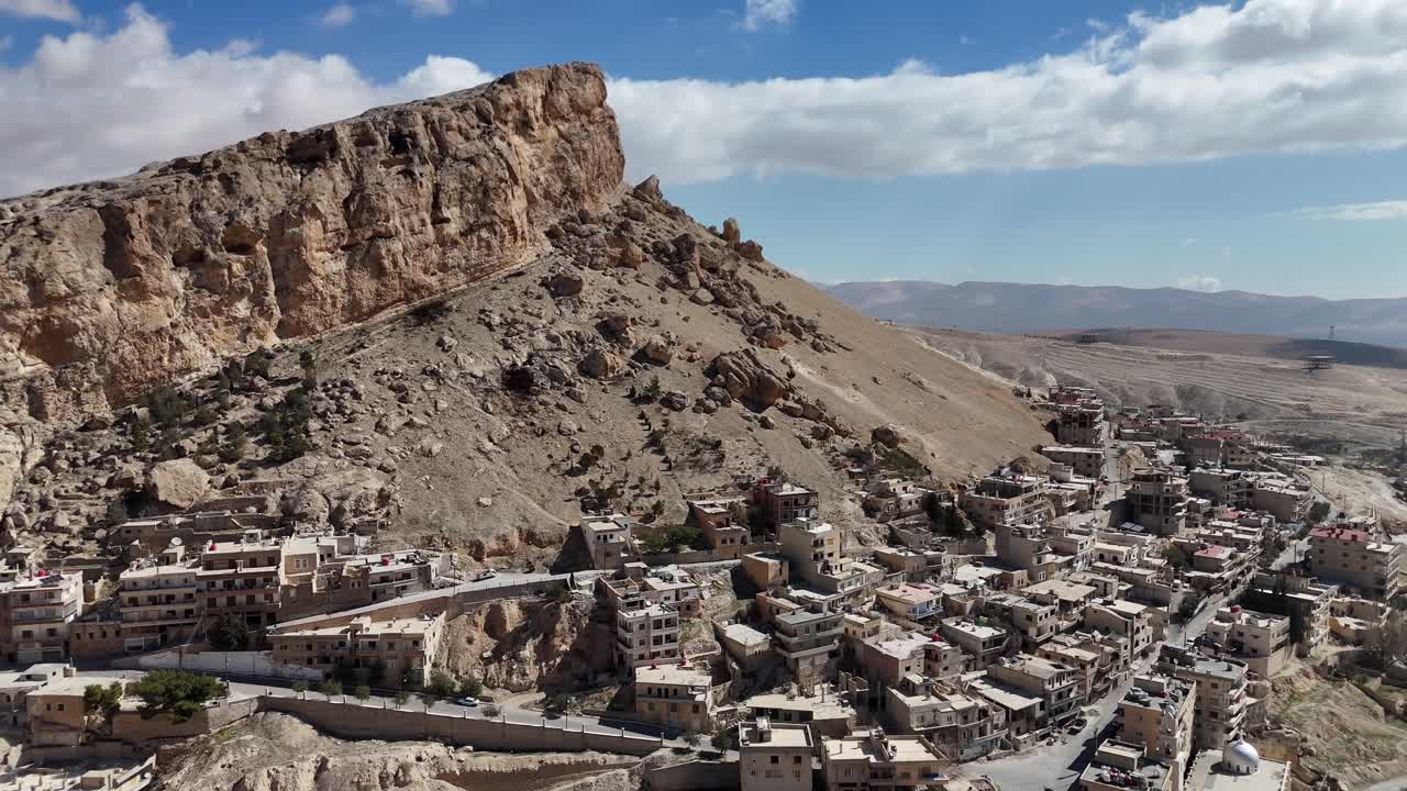 aerial drone of ancient settlement of Ma'loula, Syria, featuring the contrast between the stone architecture and the vast, barren mountain landscape