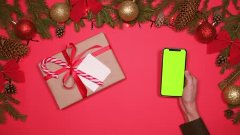mano sosteniendo un teléfono inteligente al lado de una caja de regalos en un piso de navidad