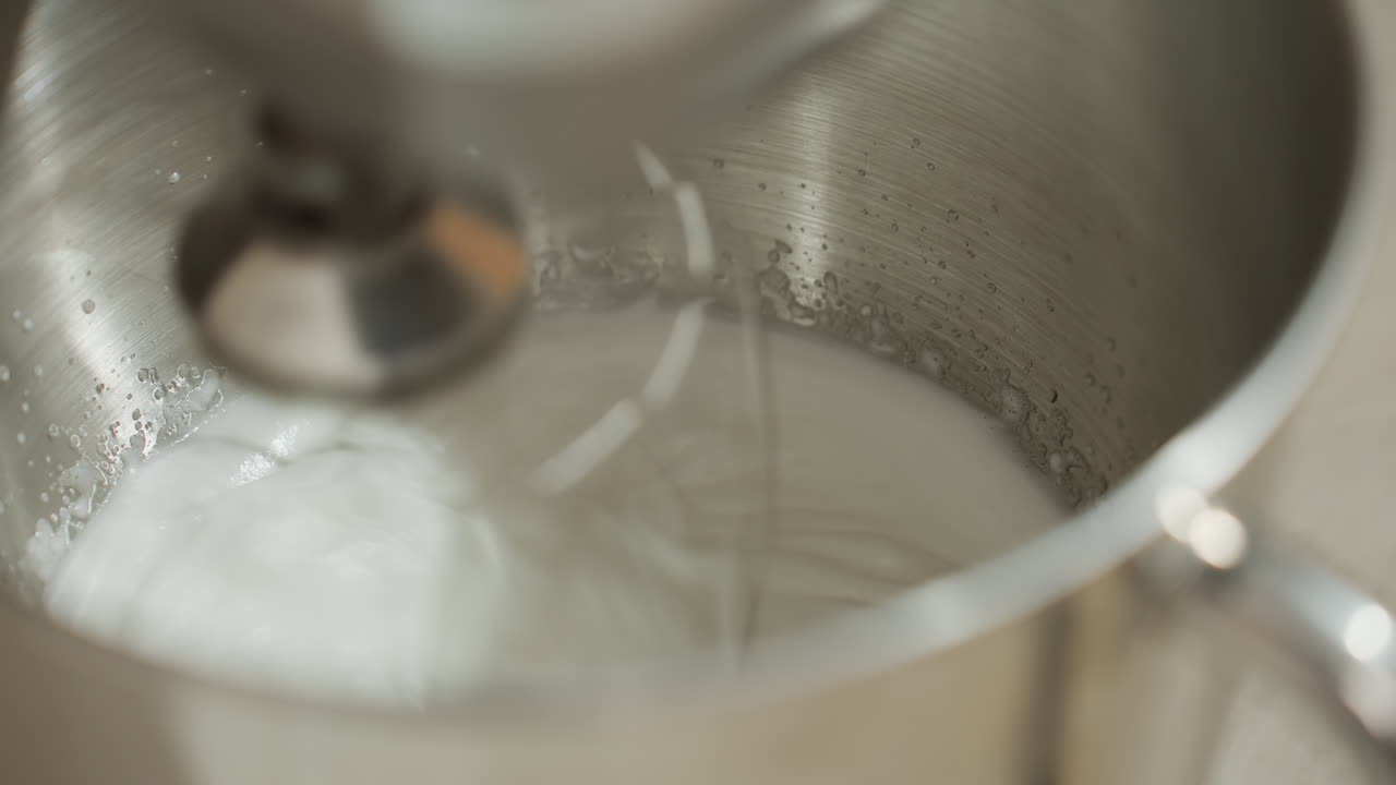 Close up of electric mixer vigorously whipping mashed ingredient inside stainless steel bowl, with visible swirl motion and creamy texture forming during high-speed blending process