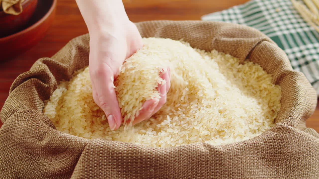 A hand interacting with and scooping rice from a burlap sack