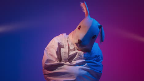 person in a straitjacket with a rabbit mask under vibrant lighting