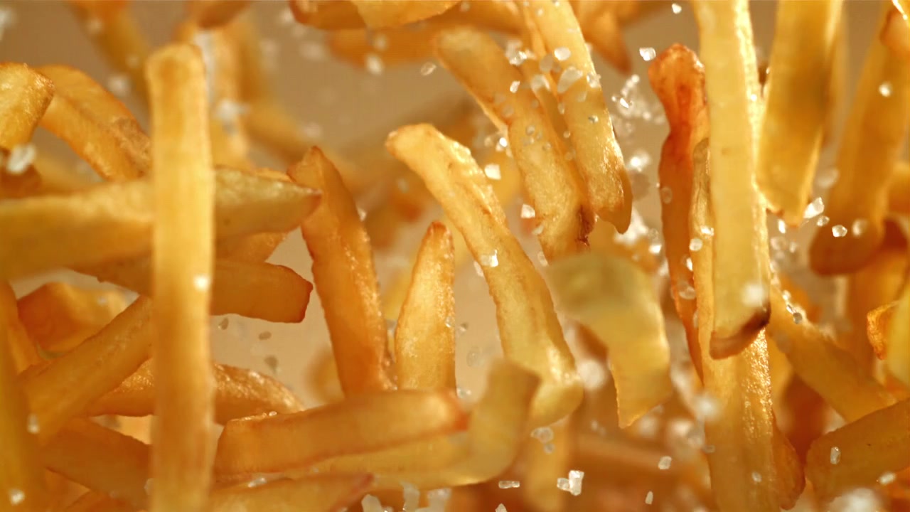 Salz fällt auf goldene Pommes Frites in Zeitlupe