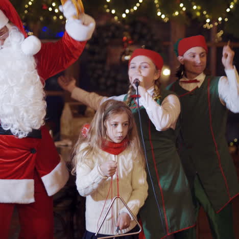 fairy characters having fun at christmas. little girl singing and dancing together with santa claus and happy elves in the decorated room.