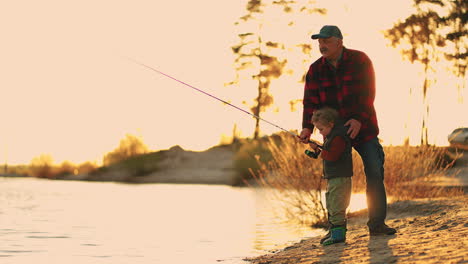 happy granddad and little grandson are catching fish by fishing rod in river in sunset