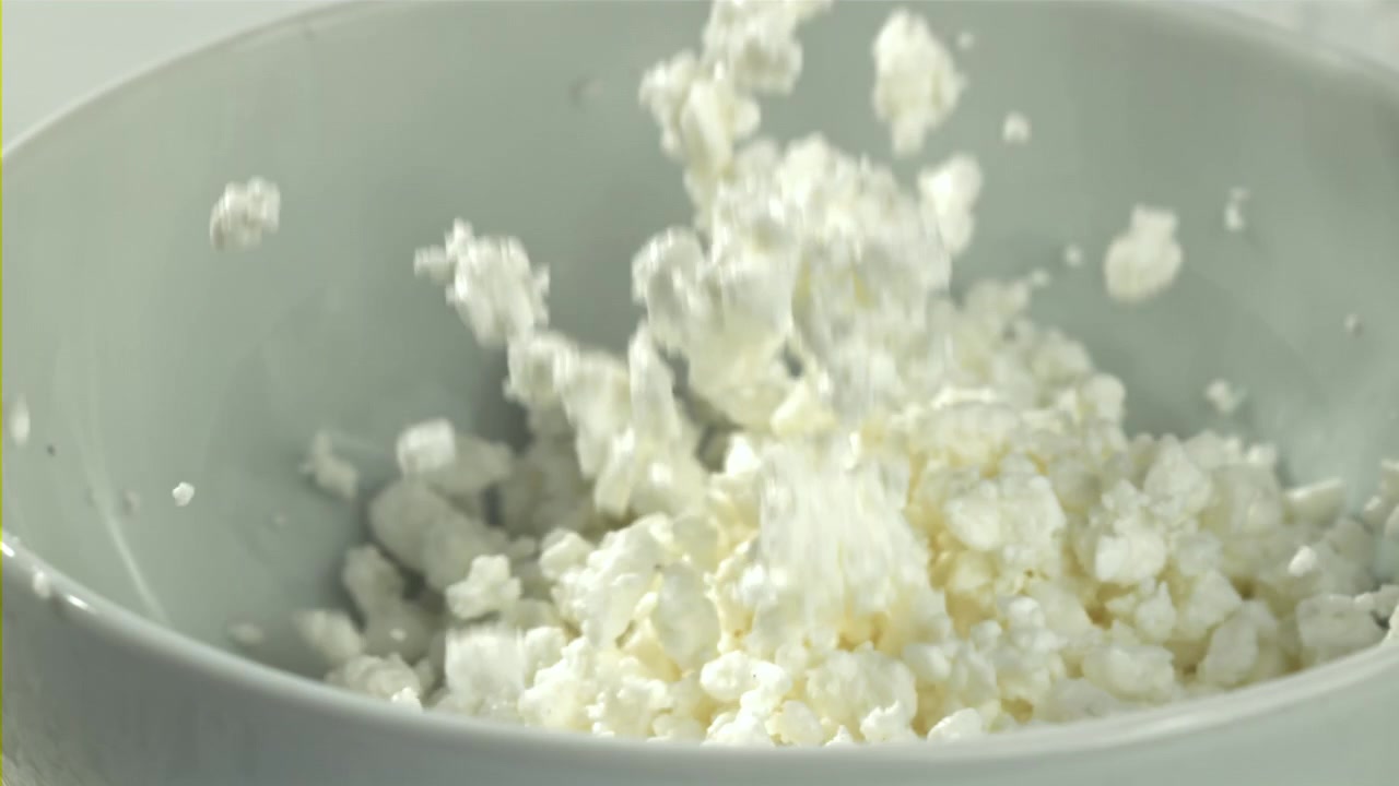 Frisk hytteost, der falder ned i en hvid skål i slowmotion