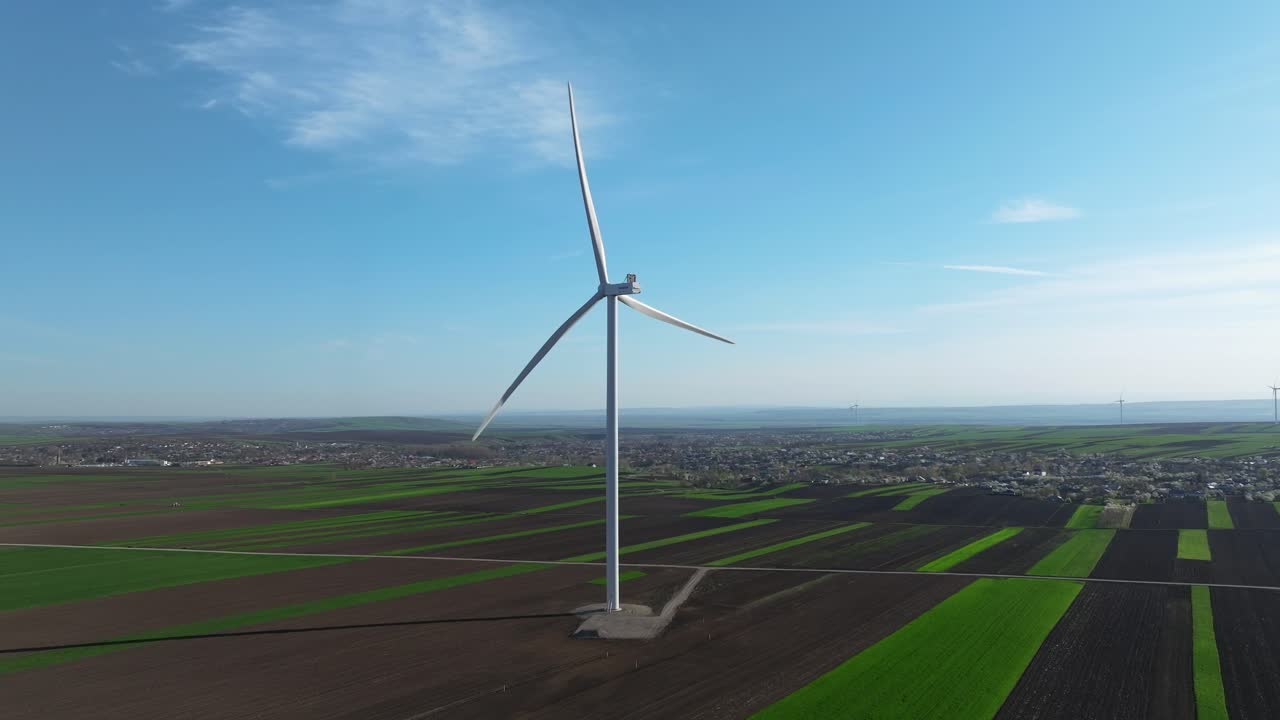 풍력 터빈은 은 파란 하늘 아래 광활한 초록색과 갈색의 농업 풍경에 높이 서 있습니다.