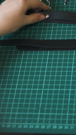 cu: skilled girl tailor makes black leather choker with fabric strips on green cutting workshop board close view