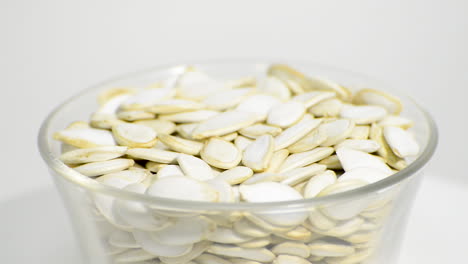 Transparent-bowl-with-pumpkin-seeds-rotating-on-a-white-background