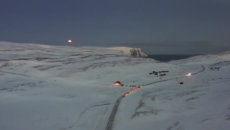 a convoy of cars waiting to go on an icy road towards the nordkapp, norway during the midwinter solstice. high to low angle towards the cars.