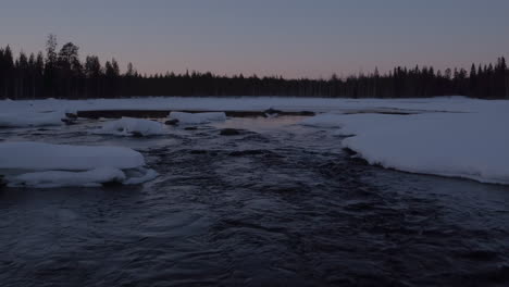 cinematic low level aerial shot of a snowy stream at dusk