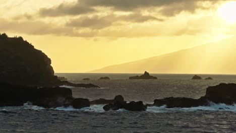 golden hour glow spreads across misty sky with ocean waves crashing on rocks in hawaii