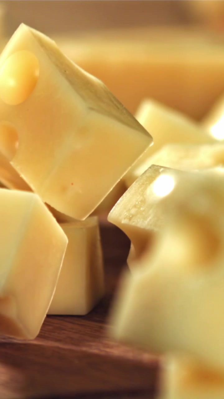 Primo piano di cubetti di formaggio giallo che cadono su un tagliere di legno.