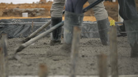 Gummistiefel-In-Nassem-Zement-Auf-Der-Baustelle,-Während-Arbeiter-Beton-Nivellieren