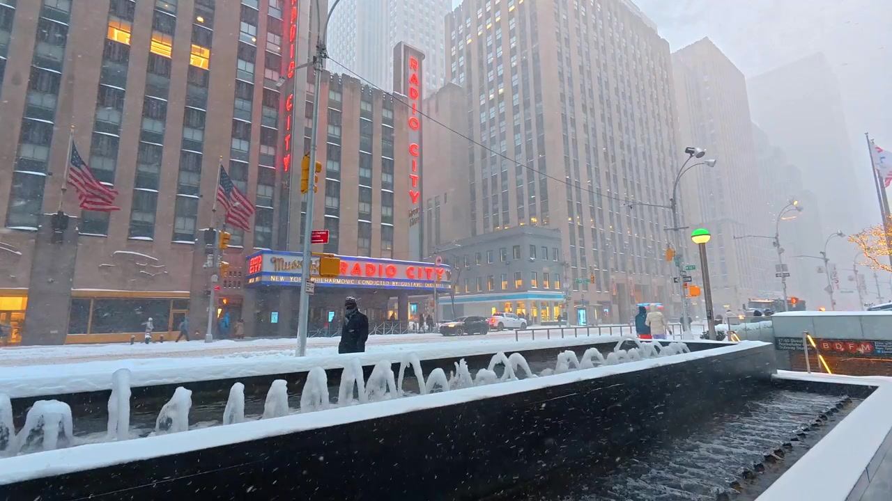 New York, USA, 25 dicembre 2025: Radio City Music Hall durante una tempesta di neve a Manhattan. Pedoni passano accanto a una fontana coperta di neve e a un ingresso della metropolitana, accanto all'insegna illuminata del teatro.