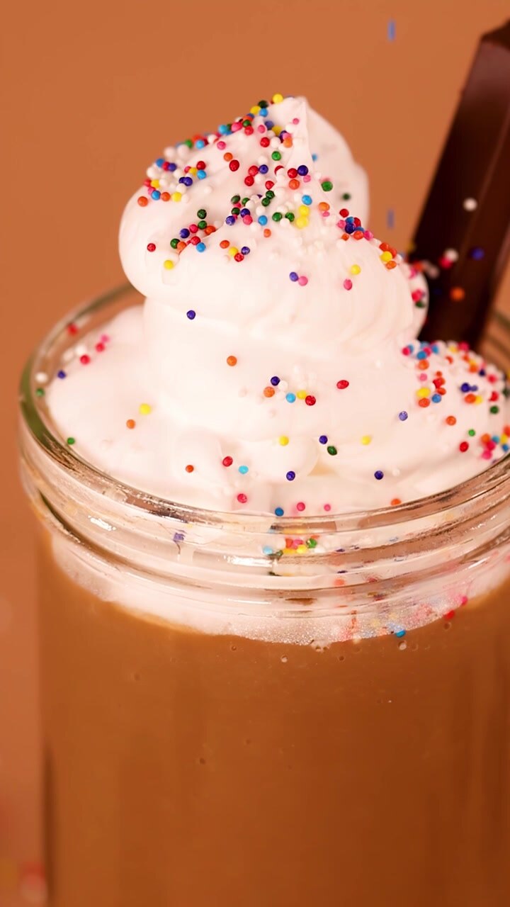 Primo piano di milkshake al cioccolato con panna montata mentre cadono zuccherini colorati su uno sfondo caldo da studio