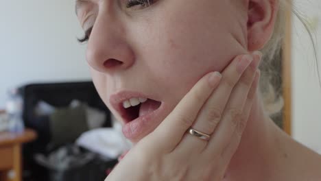 close-up of a woman holding her cheek and reacting to tooth pain. the facial expression and hand gesture indicate discomfort, possibly from dental or gum issues
