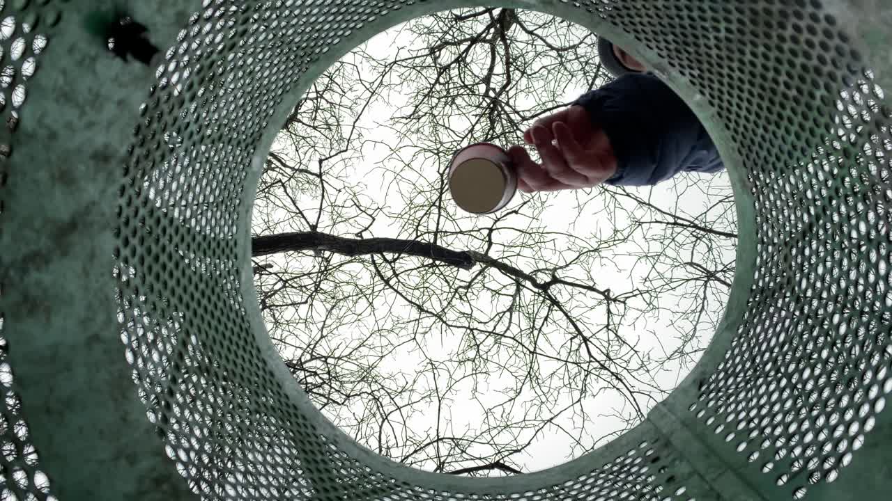 Throwing disposable coffee cup into public metal trash can on the street