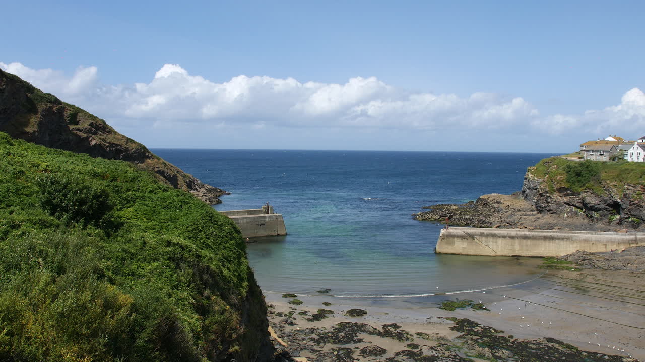 A harbor in Port Isaac, Cornwall, with fishing boats scattered across the exposed tidal sand and traditional cottages overlooking the bay. Portwenn village along the rocky coastline