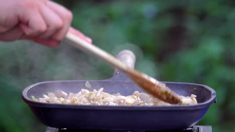 agregando tomates a la sartén de pollo en la estufa de camping