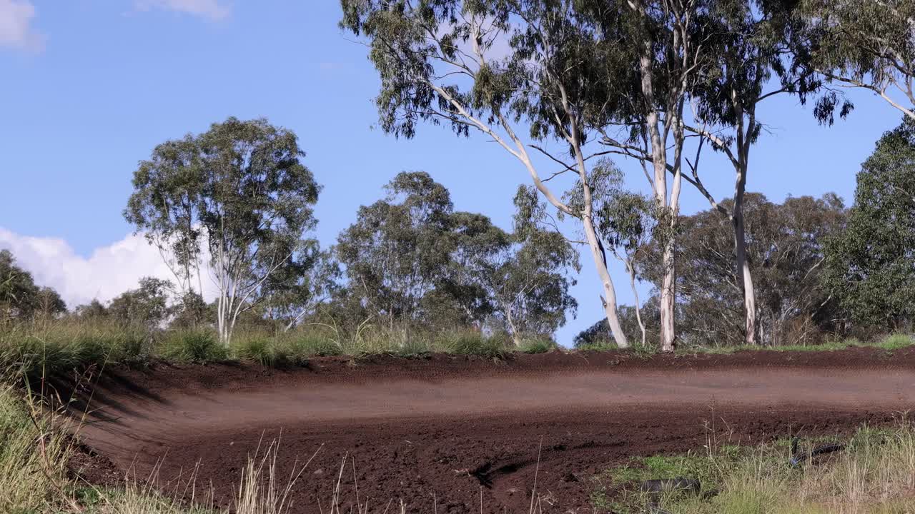A motorcyclist skillfully maneuvers a dirt bike around a forested track curve under a clear sky.