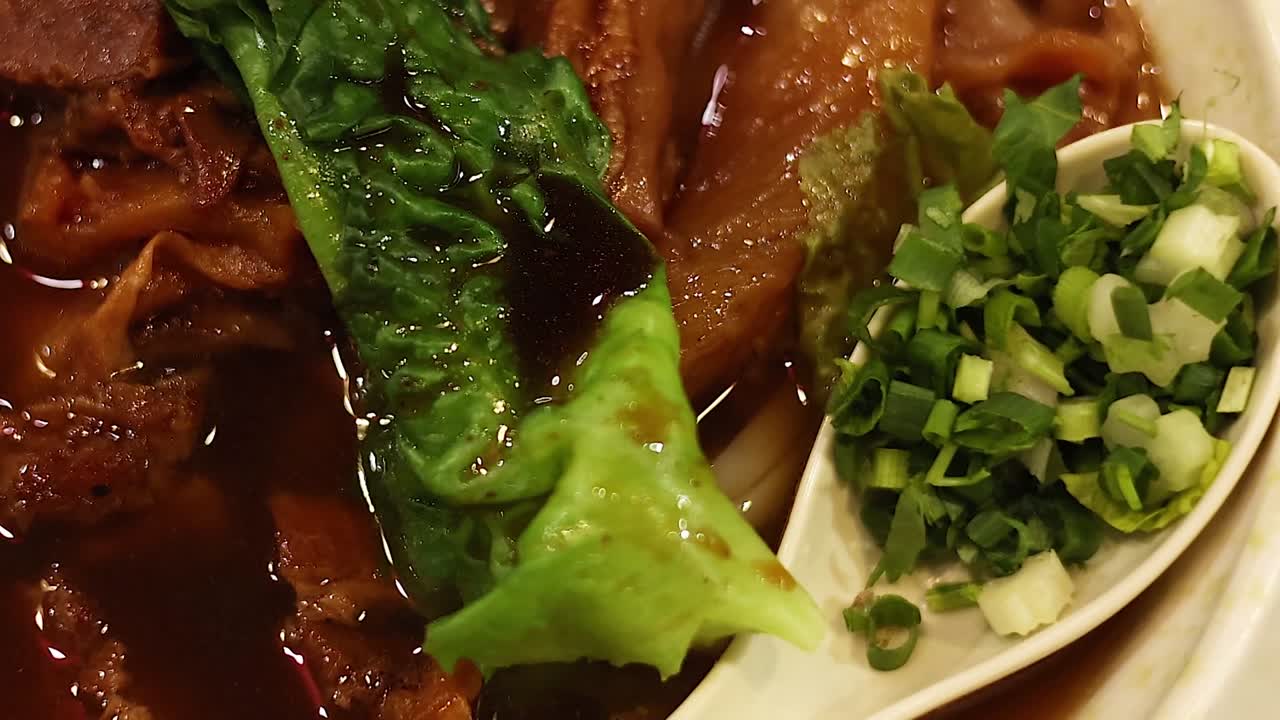 A detailed view of leafy greens with sauce, chopped scallions, and rich broth.