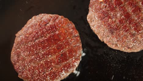 fried burger meat with bubbles of oil in a frying pan.