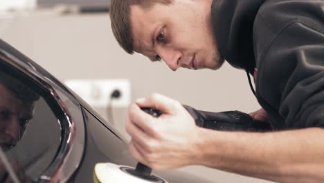 imágenes en primer plano de un joven trabajador que cuida un coche negro nuevo, pulíndolo para lograr un brillo brillante.