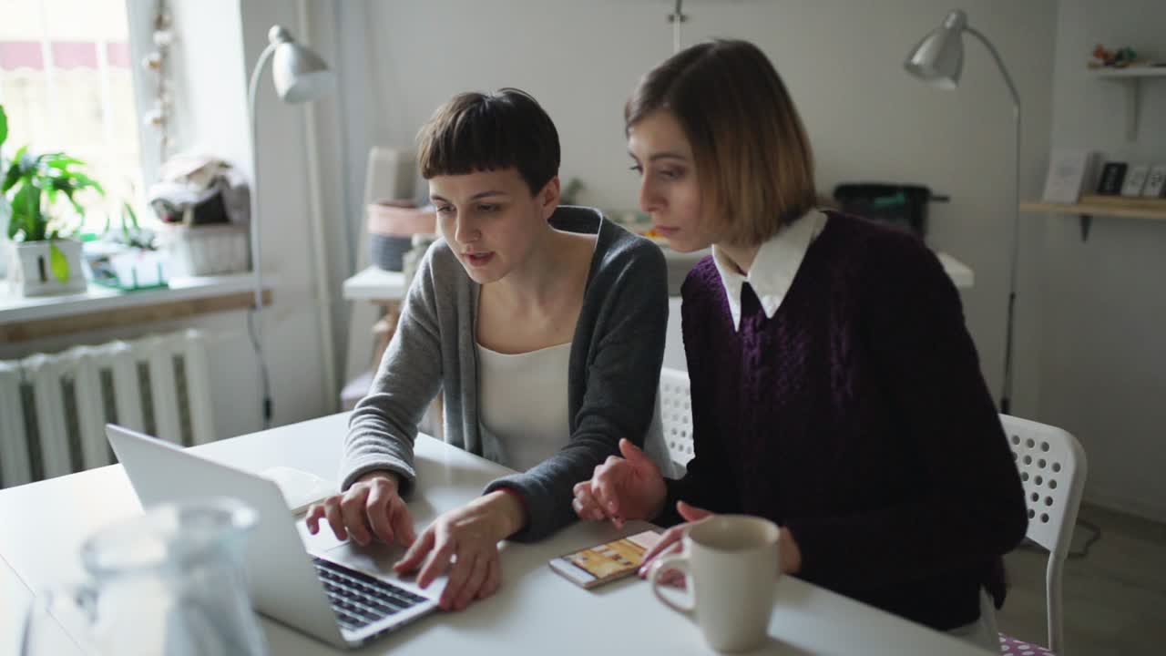 dos amigas usando un cuaderno sentadas en la mesa