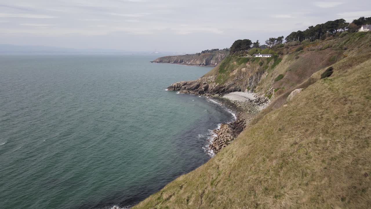 revelación aérea de una pequeña playa escondida en howth, dublín, irlanda, con una vista lejana de la cabaña bailey en el acantilado.