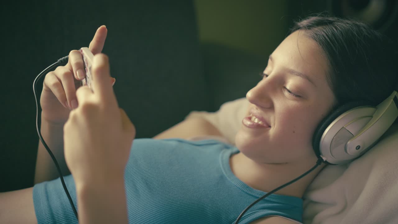 Teen girl relaxing at home, listening to music with headphones and using her smartphone. A calm, intimate moment of digital leisure in a cozy setting.