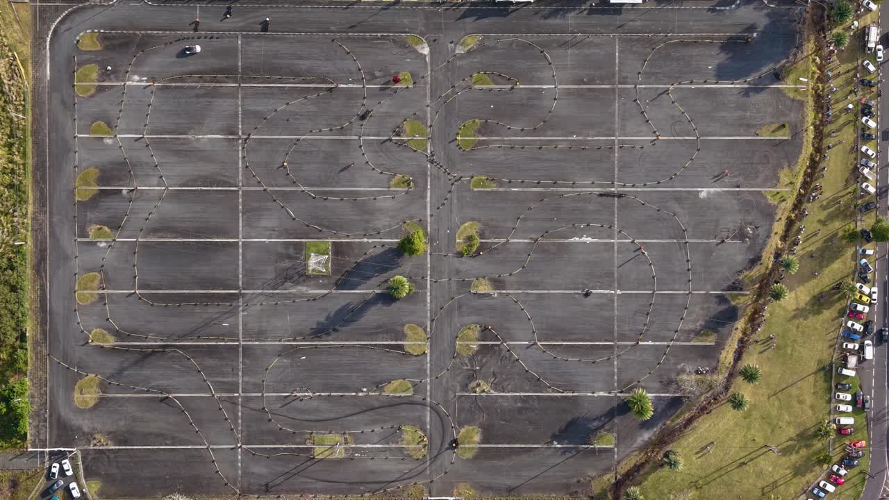 Still top-down drone shot of a car racing event at a parking lot in Mauritius, showing winding track patterns and a white vehicle navigating the course