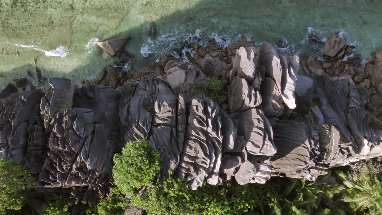 Drammatica ripresa aerea in risalita che mostra antichi massi di granito che incontrano acque cristalline turchesi e una giungla lussureggiante ad Anse Grosse Roche, La Digue, Seychelles 002 30fps