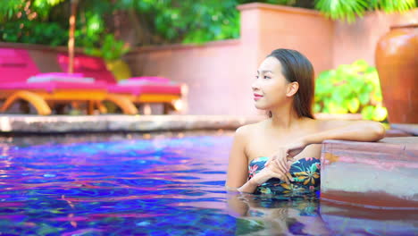 hot asian girl smile at somebody from inside the swimming pool of a topical luxury hotel in thailand