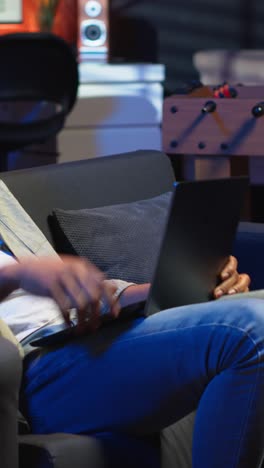vertical video adult guy typing on laptop laying on couch in stylish apartment