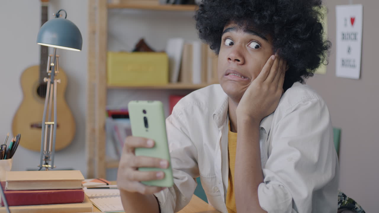 Teenager looking at a smartphone with a surprised expression at a desk.