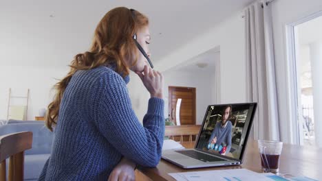 caucasian woman using laptop and phone headset on video call with male colleague