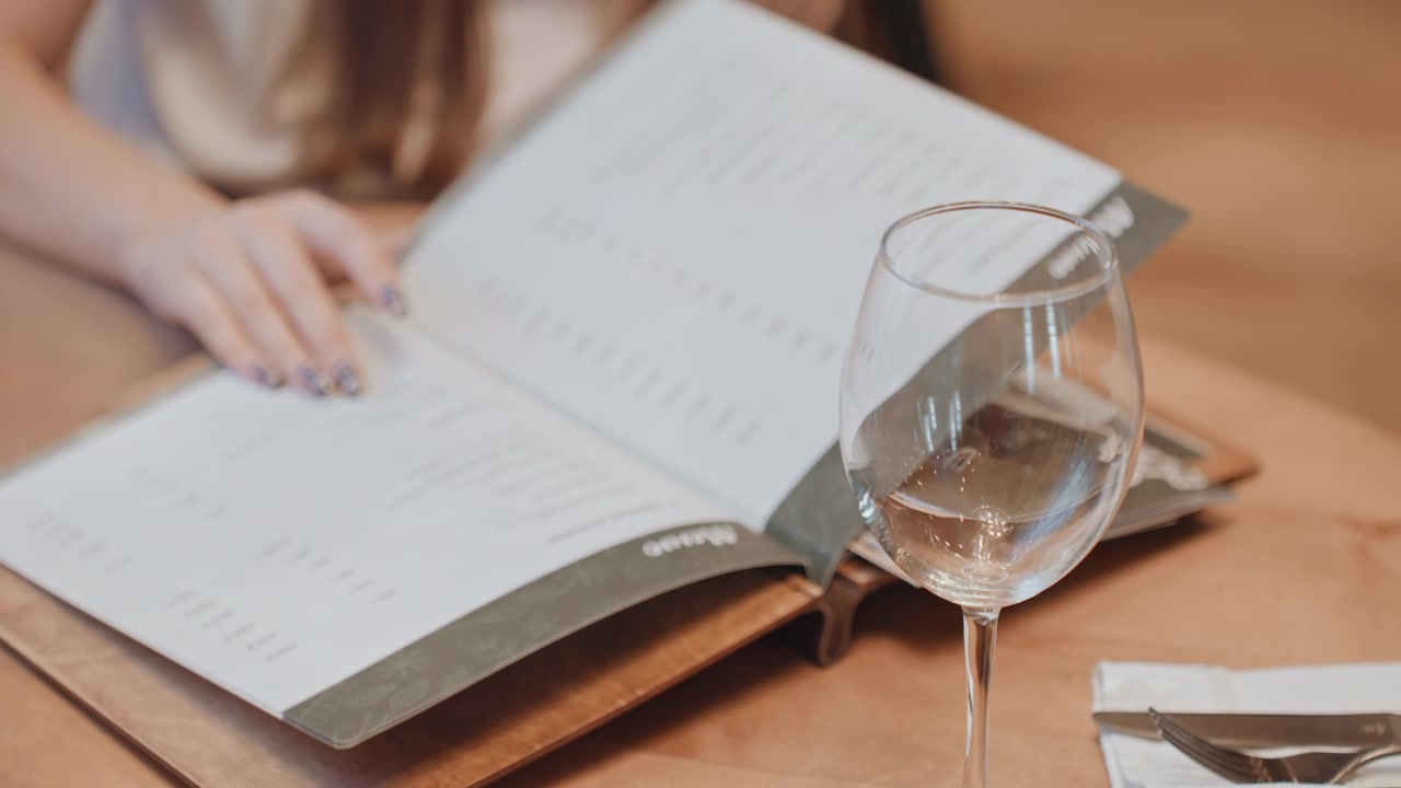 Stille aftenmiddagsscene med afslappet kvinde. Fredfyldt bistro-miljø, hvor kvinden tålmodigt gennemgår menuen. Roligt middagsmiljø, hvor kvinden eftertænksomt studerer menuen under blød belysning.