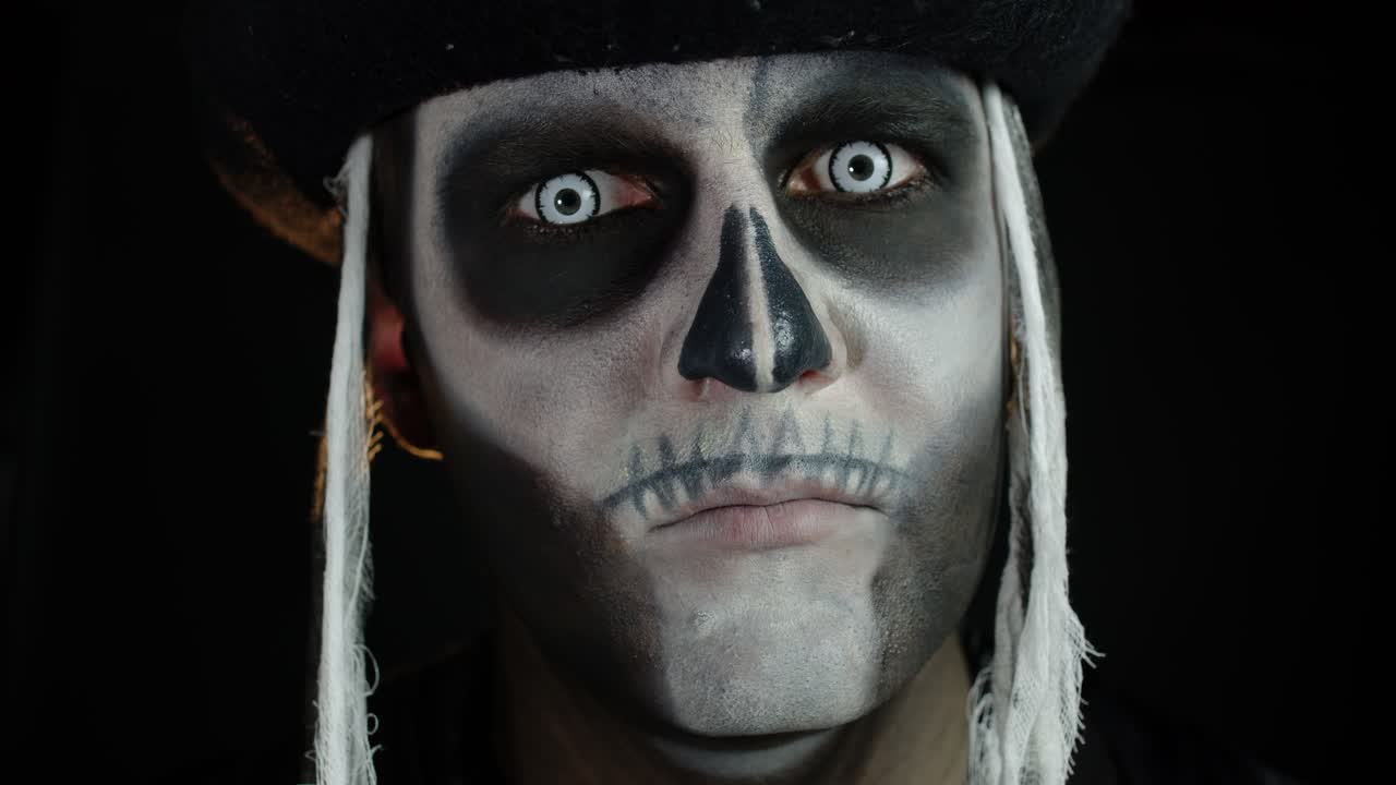 hombre aterrador con maquillaje de carnaval de esqueleto de halloween abriendo los ojos contra un fondo negro