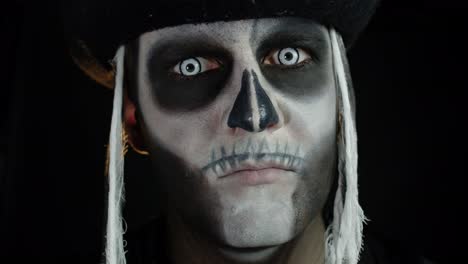 scary man with carnival makeup of halloween skeleton opening his eyes against black background