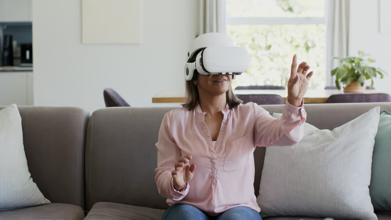 Donna con visore VR bianco, risponde a un comando e tocca oggetti virtuali sul divano.