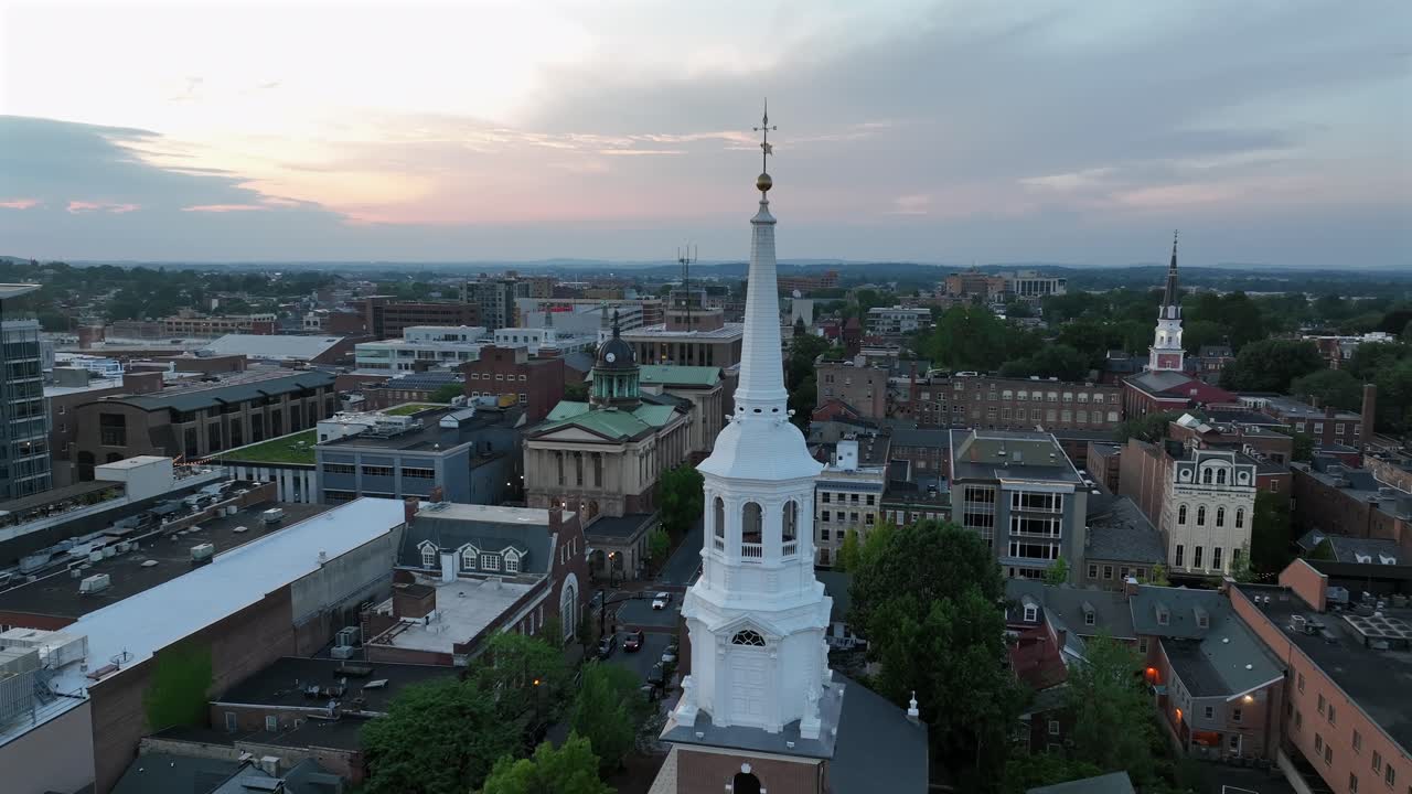 White church tower in downtown of Lancaster, Pennsylvania at dusk. Aerial passing by shot. Courthouse with cupola and other historic buildings in center of American town. Wide shot