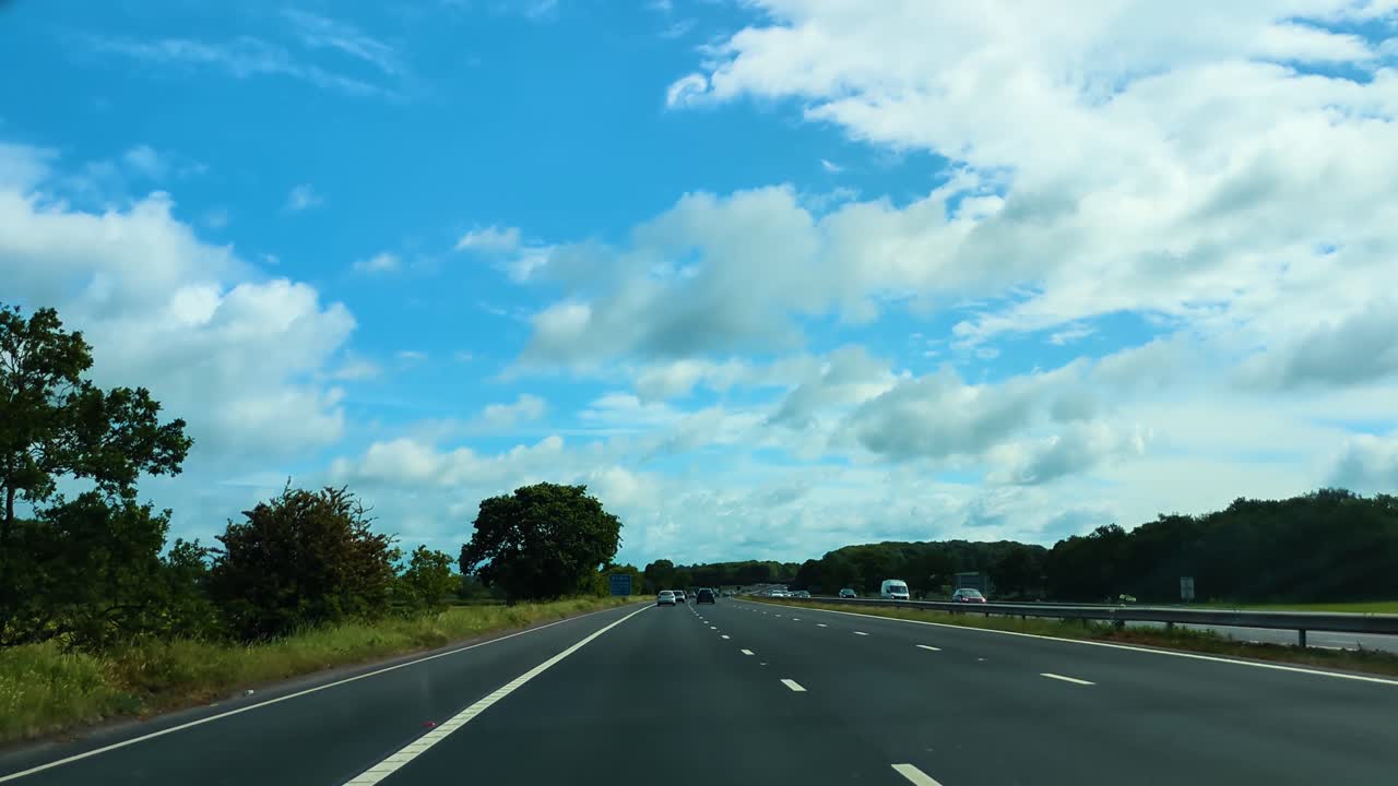POV Car Dashcam on Slip Road Entering M5 Motorway in South West England with Bright Blue Sky with Trees and Other Transportation Vehicles including Cars and Trucks.