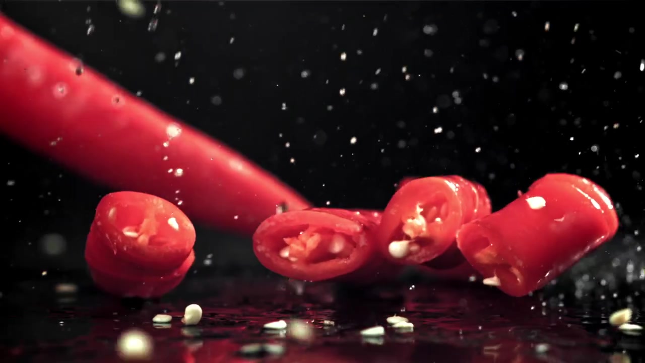 Red Chili Peppers Splashing with Water and Seeds in Slow Motion
