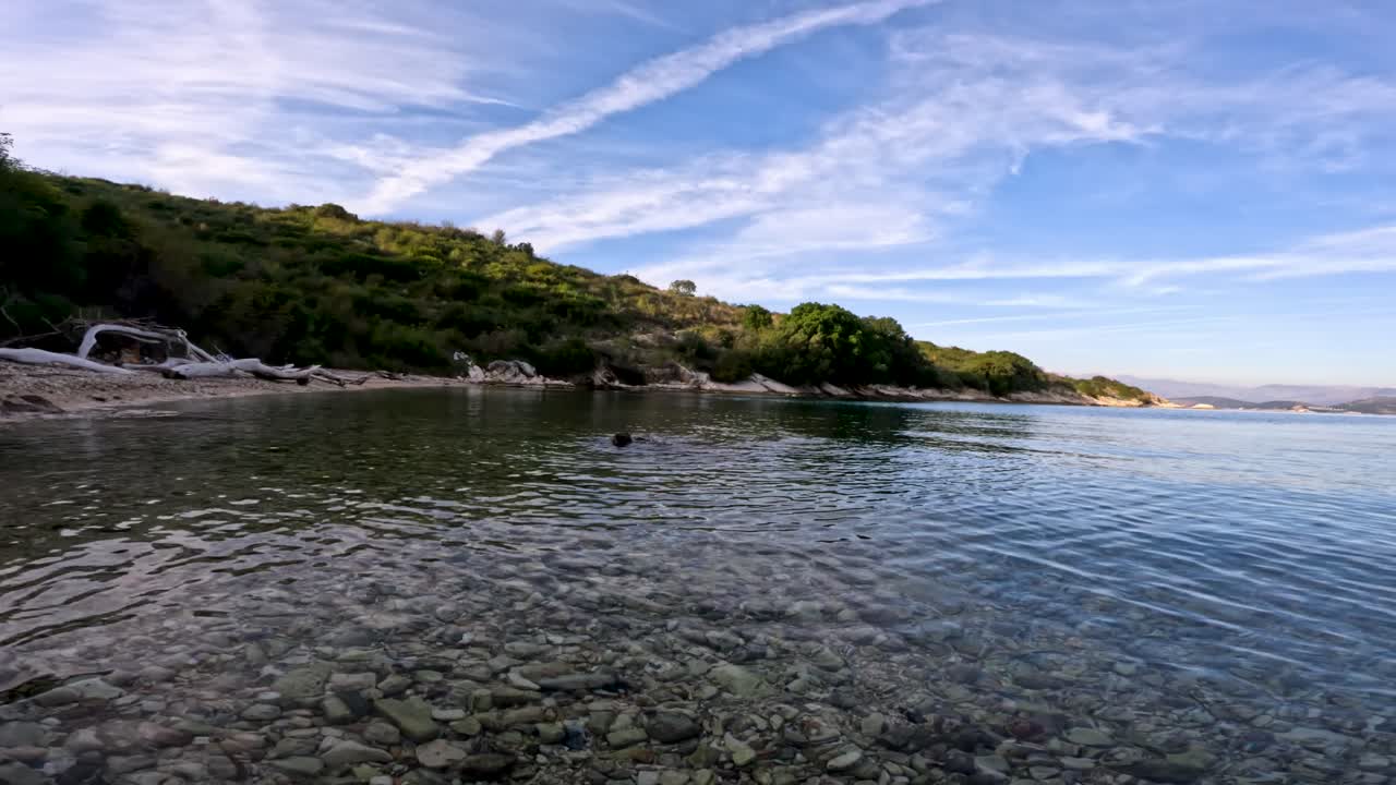 Split-Level-Aufnahme von Pebble Beach und Unterwasserfelsen mit klarem blauem Himmel und grünen Hügeln